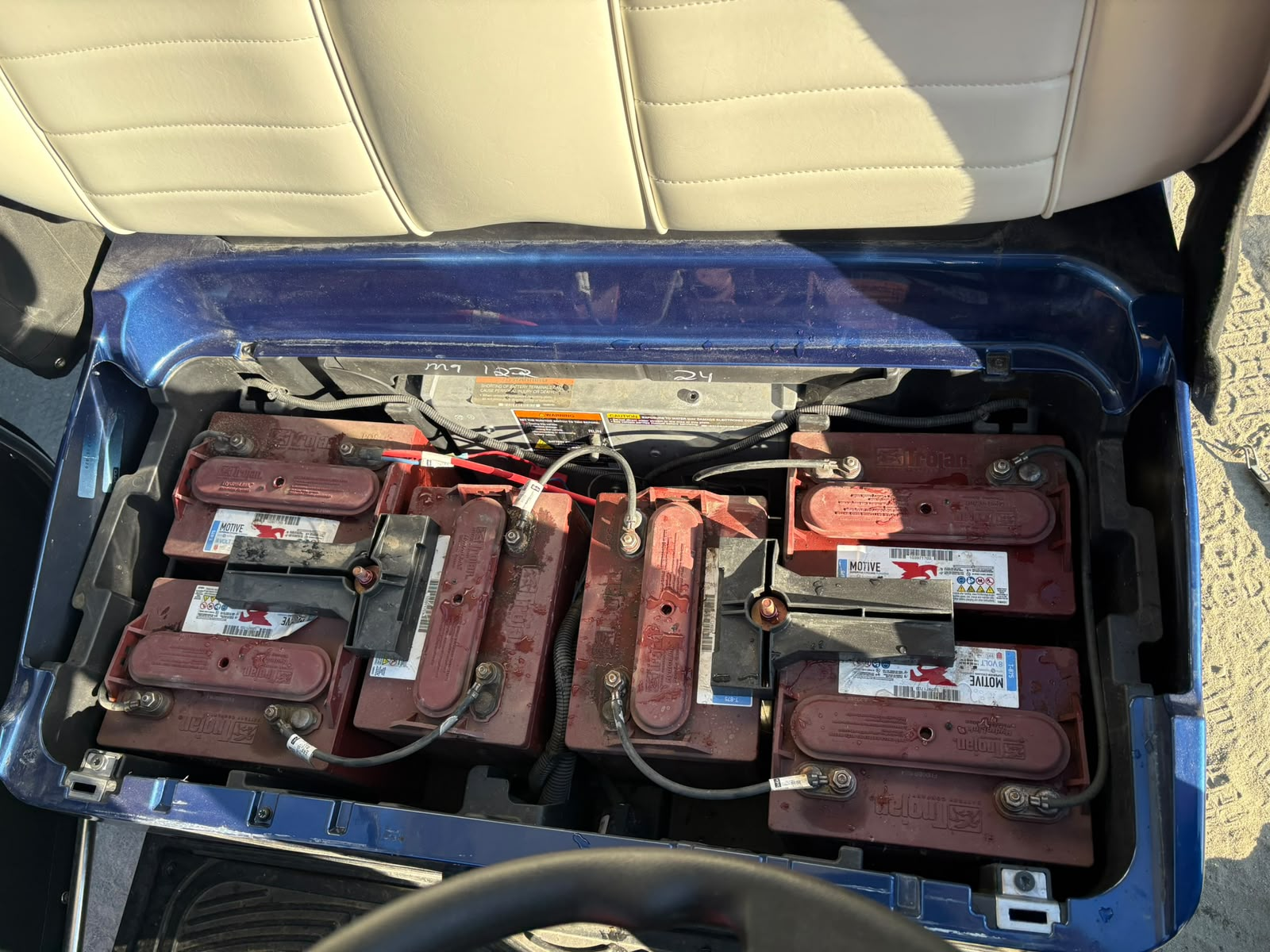 Golf cart battery bay before conversion, filled with six red lead-acid batteries and cables