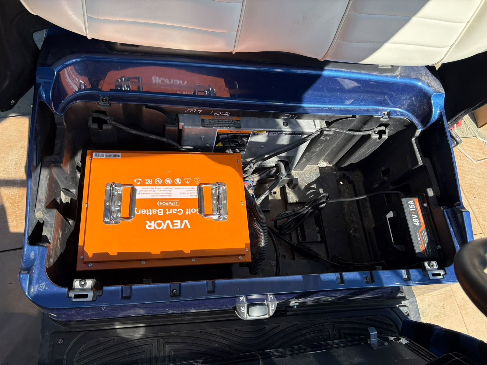 Same golf cart battery bay after conversion, with a single orange lithium battery and charger installed